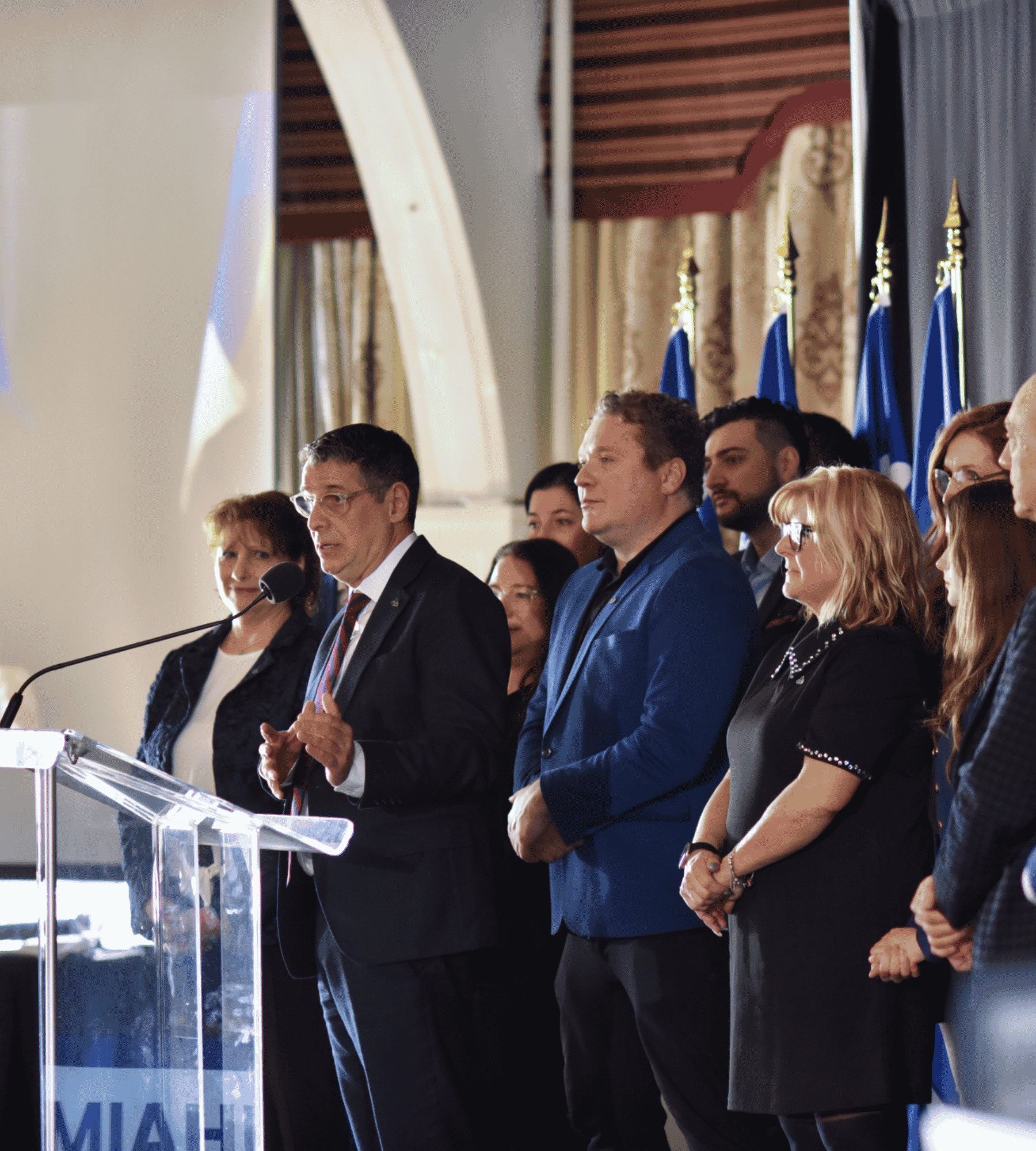 People speaking at a press conference with Quebec flags in the background